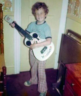 Matt Torrence as a child holding a white guitar